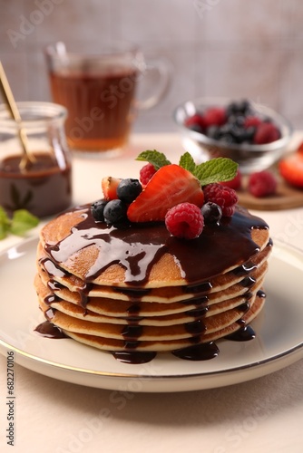 Stack of tasty pancakes with fresh berries, chocolate sauce and mint on white table, closeup