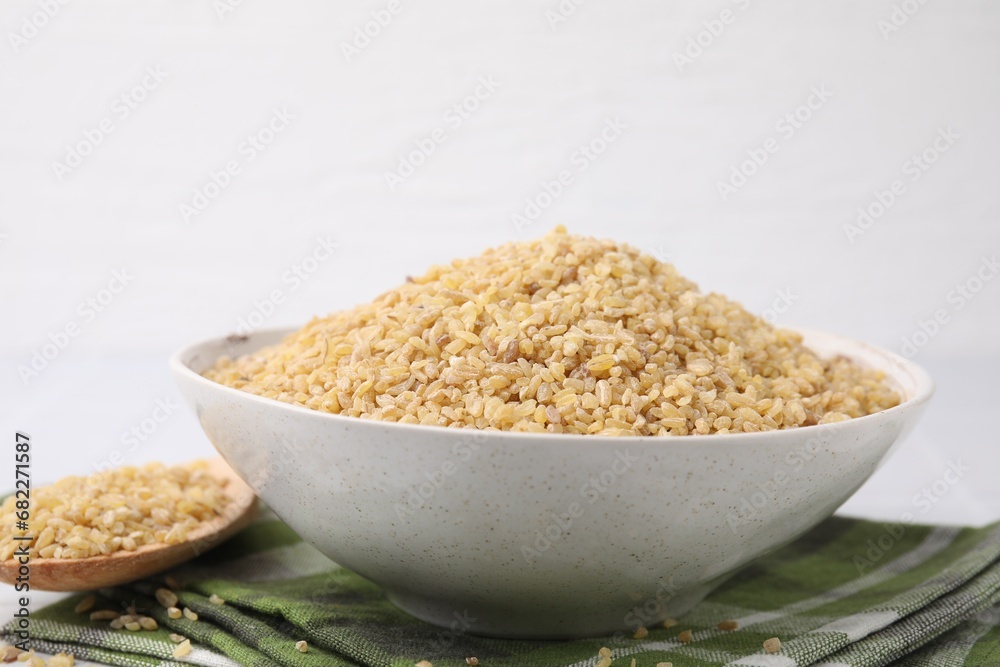 Bowl and spoon with raw bulgur on table against white background, closeup Bowl and spoon with raw bulgur on table against white background, closeup