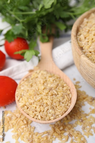 Spoon with raw bulgur and tomatoes on table, closeup