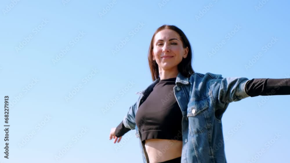 Beautiful woman looking at camera and spinning on blue sky background. Happy circling person hands in sides. Success concept. Excited moments. Victory lifestyle. Positive girl. Side view. Slow motion. Beautiful woman looking at camera and spinning on blue sky background. Happy circling person hands in sides. Success concept. Excited moments. Victory lifestyle. Positive girl. Side view. Slow motion.
