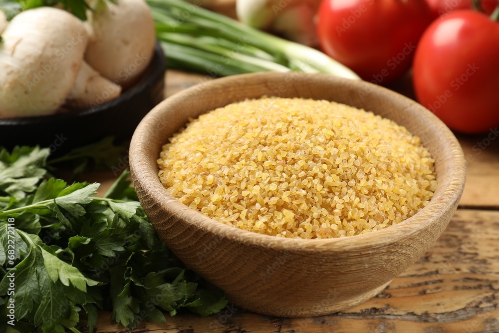 Raw bulgur in bowl, parsley and vegetables on wooden table, closeup Raw bulgur in bowl, parsley and vegetables on wooden table, closeup