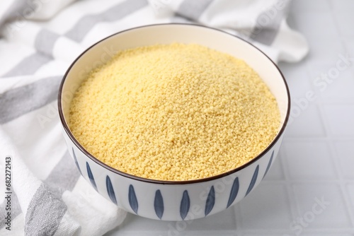 Raw couscous in bowl on white tiled table, closeup