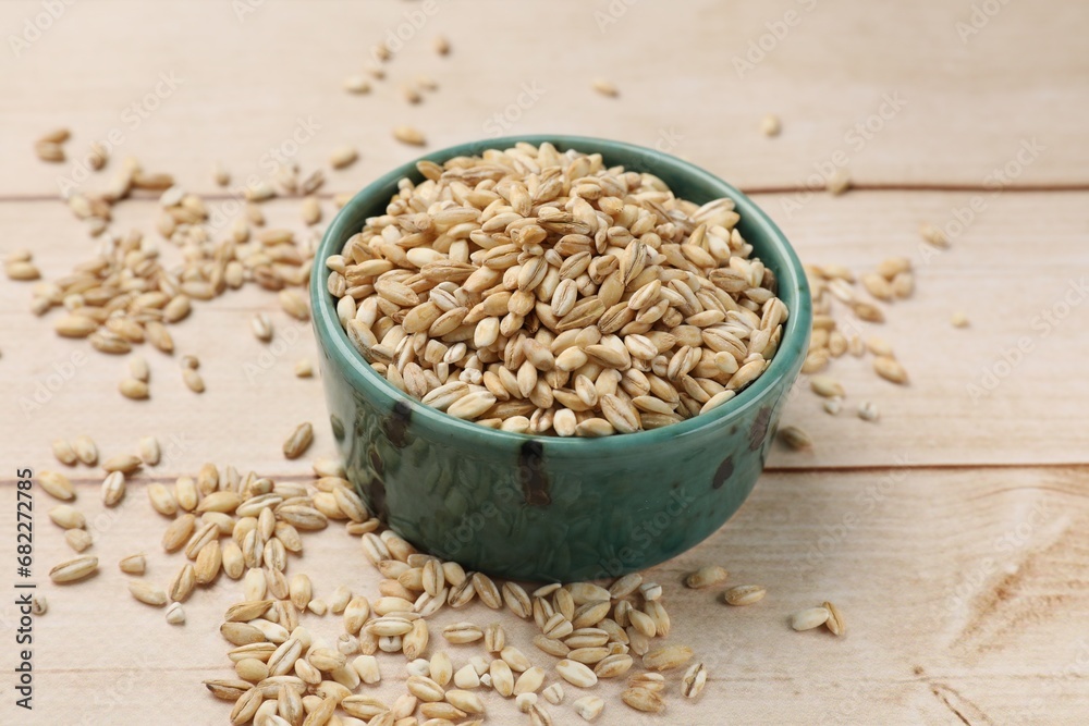 Dry pearl barley in bowl on light wooden table, closeup