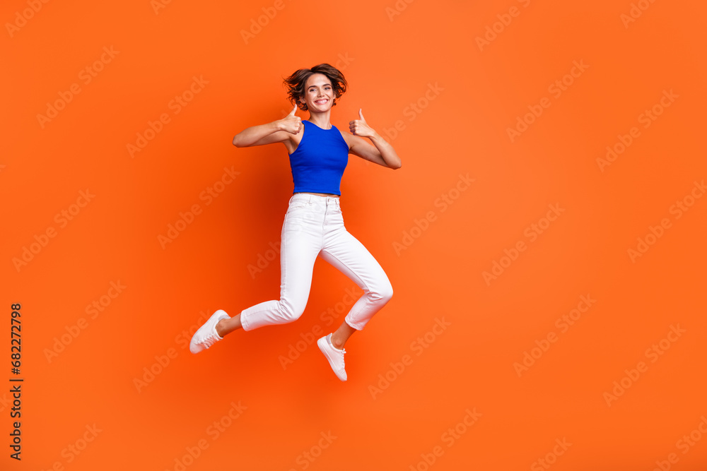 Full body photo of active carefree lady jump demonstrate thumb up empty space ad isolated on orange color background
