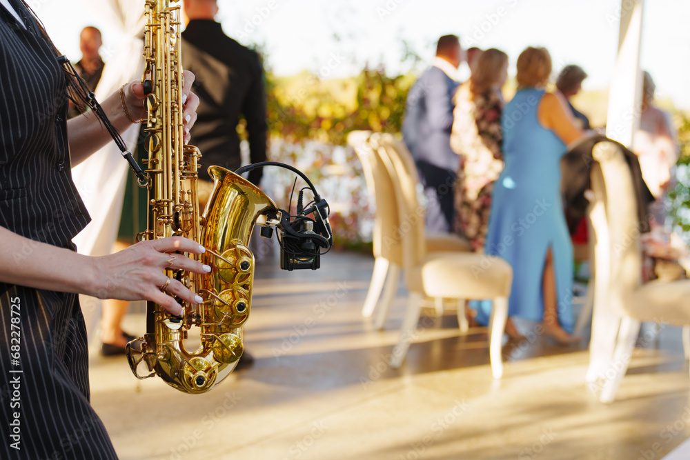 A woman musician plays the saxophone at an open-air party.  - obrazy, fototapety, plakaty 