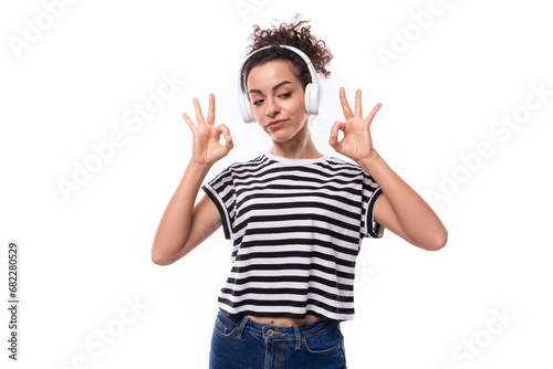 young positive curly brunette woman in a striped casual t-shirt listens to music in headphones