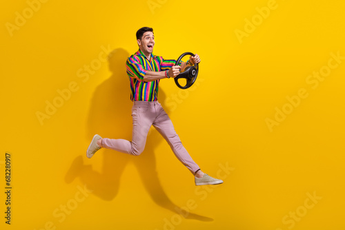 Full body length photo of crazy guy jumping with steering wheel without automobile driver license isolated on yellow color background