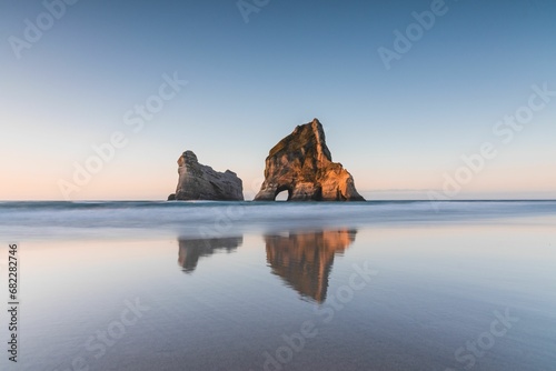 Serene beach scene featuring two large cliffs in the distance. Wharariki Beach, New Zealand