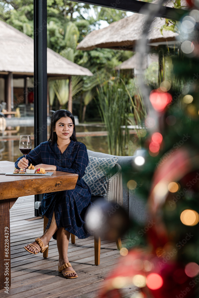 Portrait of single asian woman sitting in restaurant with a glass of wine celebrating Christmas or New Year eve with Christmas tree in foreground Portrait of single asian woman sitting in restaurant with a glass of wine celebrating Christmas or New Year eve with Christmas tree in foreground