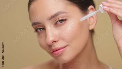 Young beautiful woman applying face serum with pipette on her face close up. Cosmetic procedures for facial skin care