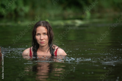 Fototapeta Naklejka Na Ścianę i Meble -  A young beautiful dark-haired girl bathes in a pond with a pit bull terrier dog.