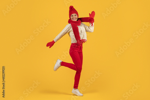 Joyful woman in red knitted hat jumping on yellow backdrop