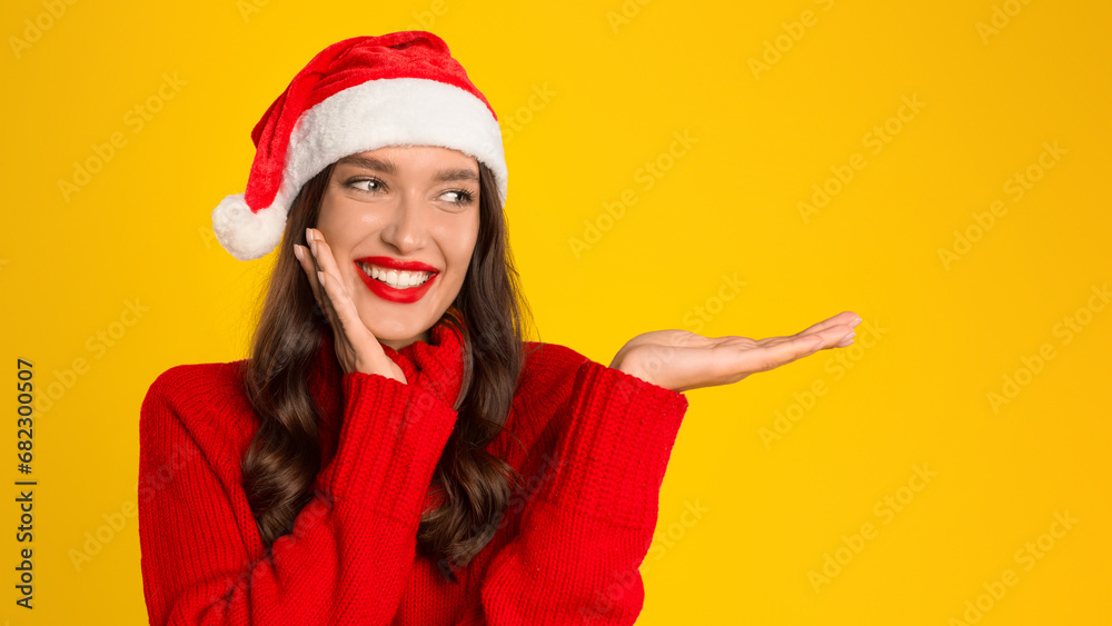 lady with open palm on yellow background, wearing Santa hat lady with open palm on yellow background, wearing Santa hat