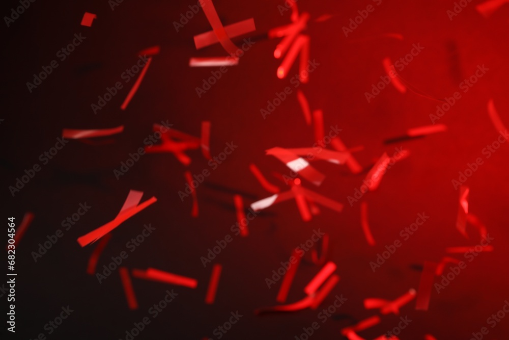 Shiny confetti falling down on dark red background