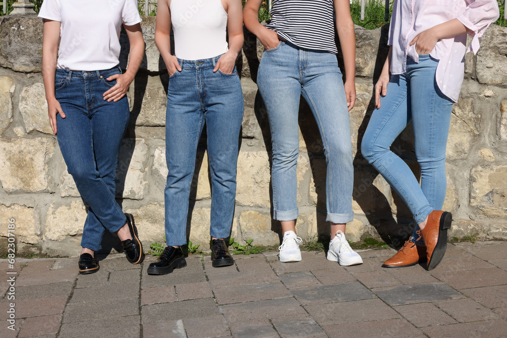 Women in stylish jeans near stone wall outdoors on sunny day, closeup Women in stylish jeans near stone wall outdoors on sunny day, closeup