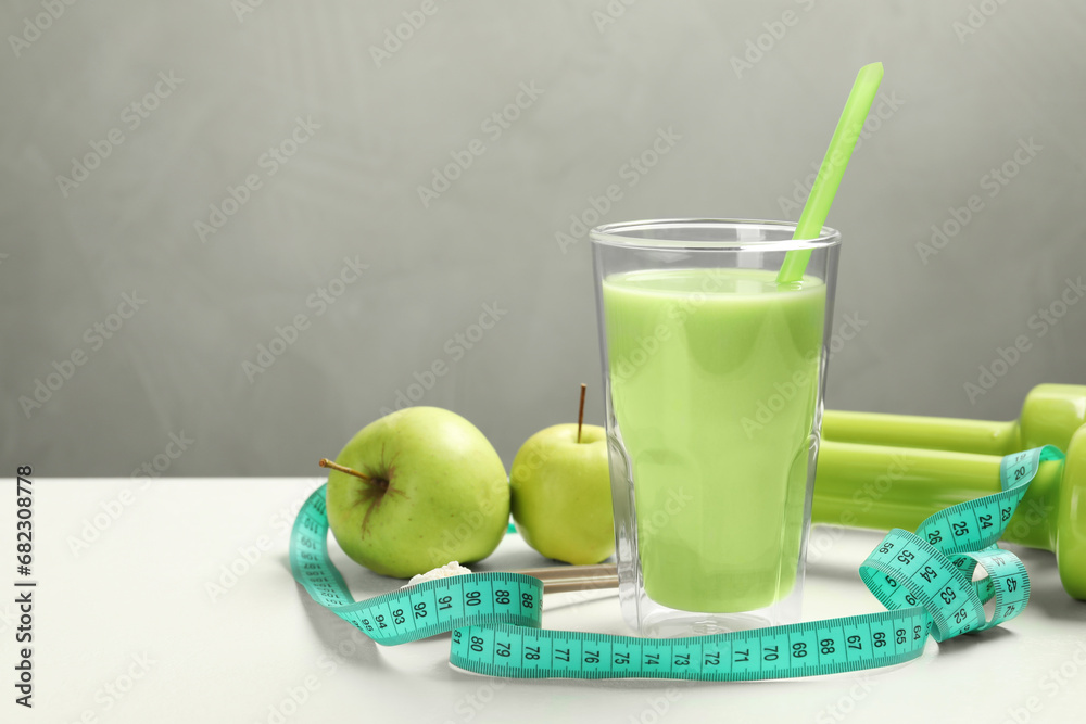 Tasty shake with apples, dumbbells and measuring tape on white table against gray background, space for text. Weight loss Tasty shake with apples, dumbbells and measuring tape on white table against gray background, space for text. Weight loss
