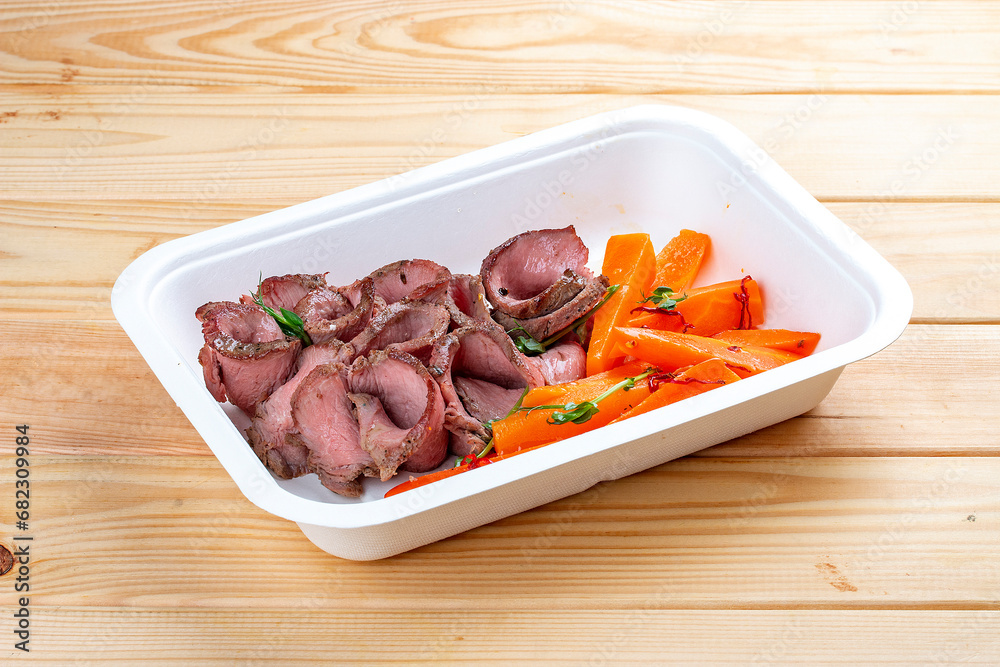 Veal sous vide with juicy carrots. Healthy diet. Takeaway food. Eco packaging. On a wooden background.
