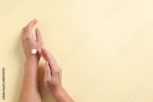 Woman applying cosmetic cream onto hand on beige background, top view. Space for text