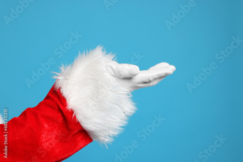 Merry Christmas. Santa Claus holding something on light blue background, closeup photo