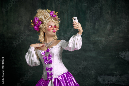 Woman dressed like classic historical character, in old-fashioned dress and taking selfie on mobile phone against vintage background. photo