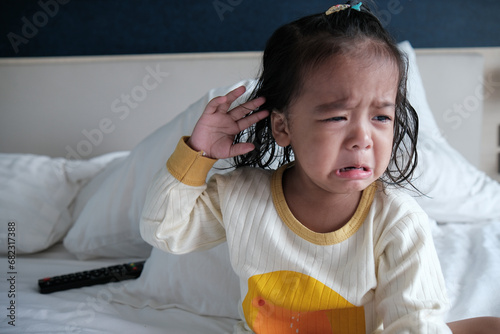 Adorable little 2 year asian girl crying on white bed