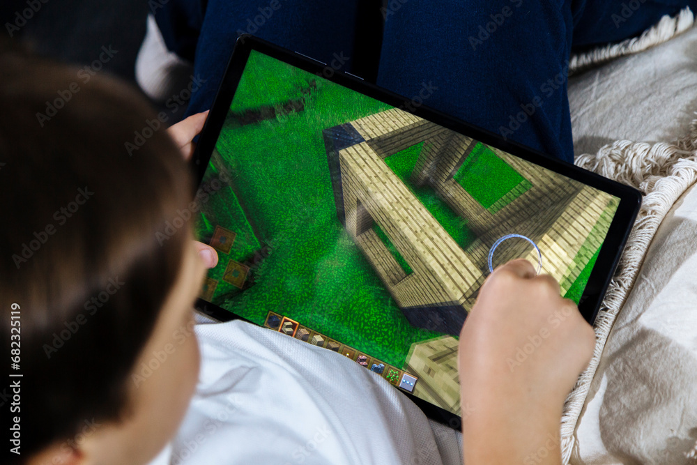 Fototapeta premium Little boy playing Minecraft game on a tablet. Minecraft is a very popular game among children and teenagers. Rosario, Argentina - November 20, 2023.