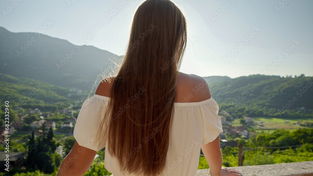 Rear view shot of brunette woman enjoying view on alley and mountains with sunset light from her villa terrace Rear view shot of brunette woman enjoying view on alley and mountains with sunset light from her villa terrace
