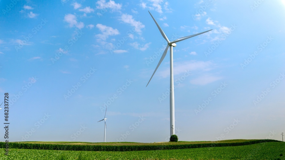 View on green fields and meadows with working wind powered turbines generating electric power View on green fields and meadows with working wind powered turbines generating electric power