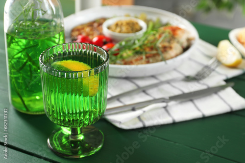 Delicious drink with tarragon in glass on green table, closeup. Space for text photo