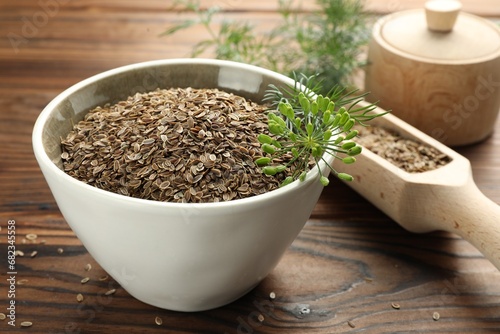 Bowl of dry seeds, scoop and fresh dill on wooden table, closeup