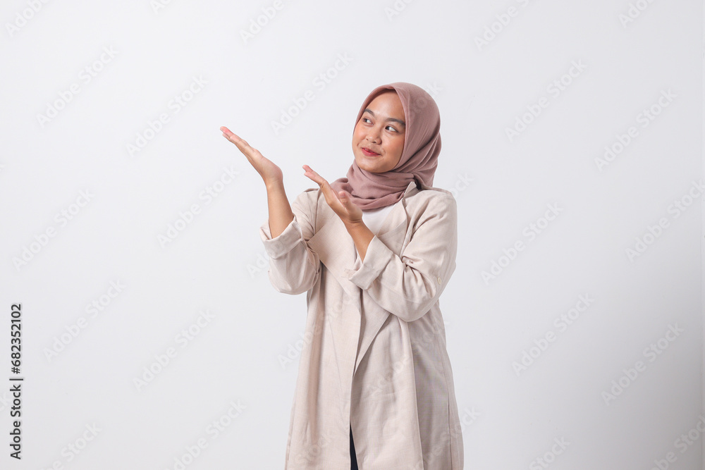 Portrait of excited Asian hijab woman in casual suit pointing and showing product in her side with finger. Businesswoman concept. Isolated image on white background Portrait of excited Asian hijab woman in casual suit pointing and showing product in her side with finger. Businesswoman concept. Isolated image on white background