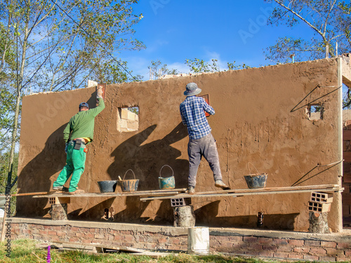 Two workers plastering a wall standing in a very rustic and unstable scaffolding, at a construction site near the town of Arcabuco, in central Colombia.