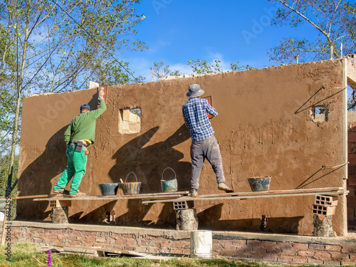 Fotografia Two workers plastering a wall standing in a very rustic and unstable scaffolding,  at a construction site near the town of Arcabuco, in central Colombia
