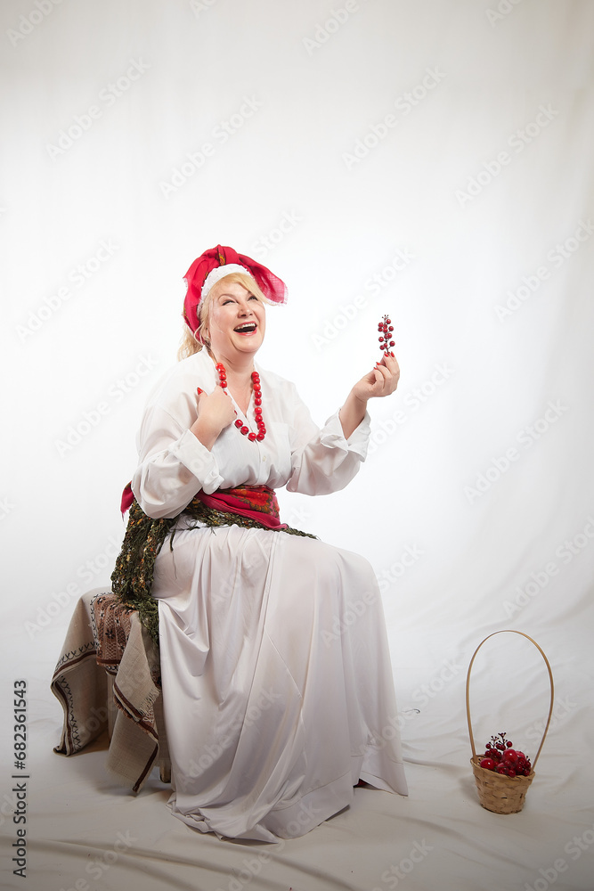 Obraz premium Portrait of heerful funny adult mature woman solokha with red berries. Female model in clothes of national ethnic Slavic style. Stylized Ukrainian, Belarusian or Russian woman in comic photo shoot