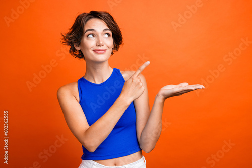 Photo of pretty dreamy girl dressed blue top open mouth looking pointing finger showing arm empty space isolated orange color background