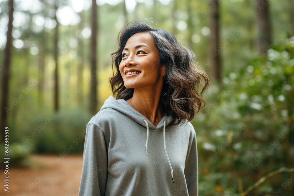Smiling Asian woman enjoying a serene walk in the forest relating to themes of wellness, leisure, and nature Smiling Asian woman enjoying a serene walk in the forest relating to themes of wellness, leisure, and nature