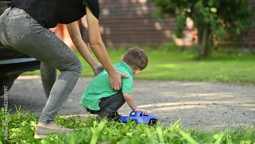 An old car without a rear view camera moves towards a child playing on the street. Mom quickly runs up and saves the little boy