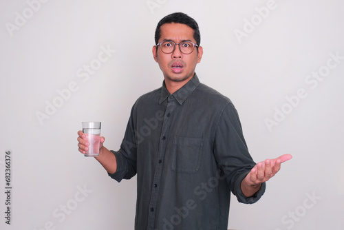 Adult Asian man holding a glass of water with worried expression