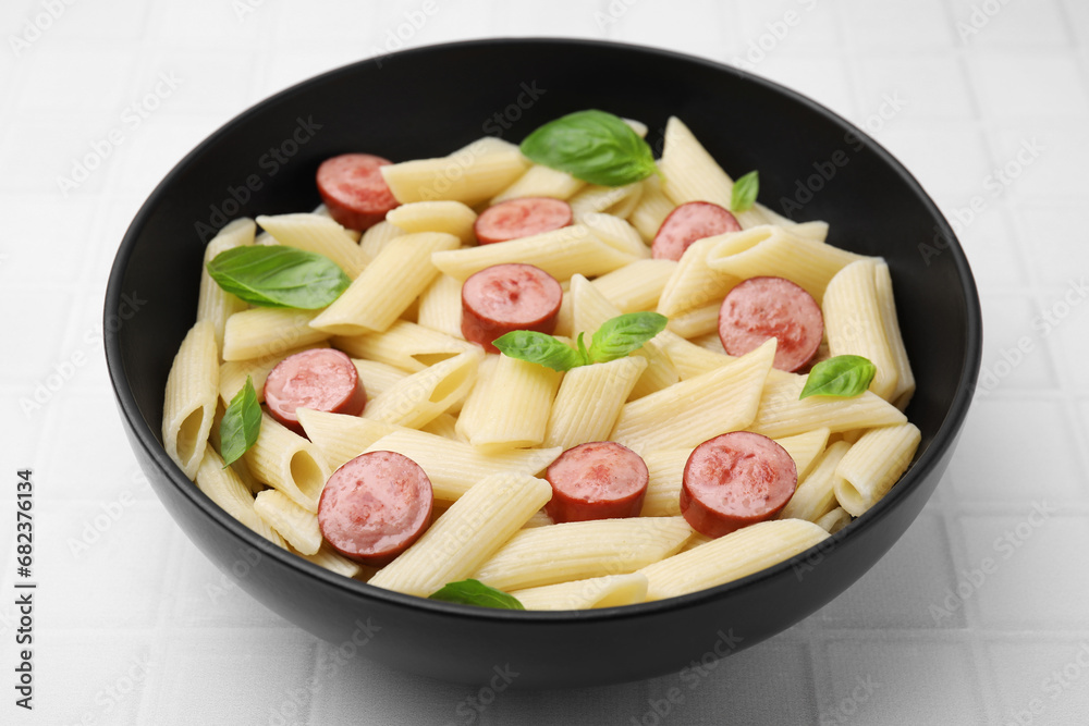 Tasty pasta with smoked sausage and basil in bowl on white tiled table, closeup Tasty pasta with smoked sausage and basil in bowl on white tiled table, closeup