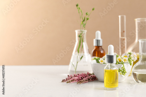 Cosmetic oil  laboratory dishware and flowers on white table  space for text