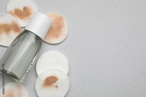 Bottle of makeup remover, clean and dirty cotton pads on light grey background, flat lay. Space for text