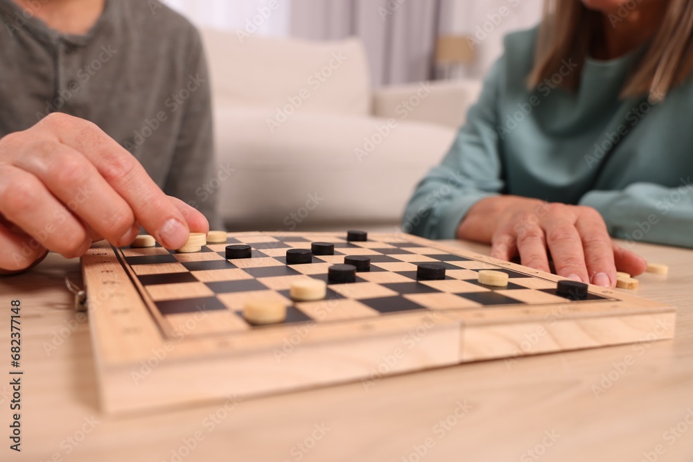 People playing checkers at wooden table in room, closeup People playing checkers at wooden table in room, closeup