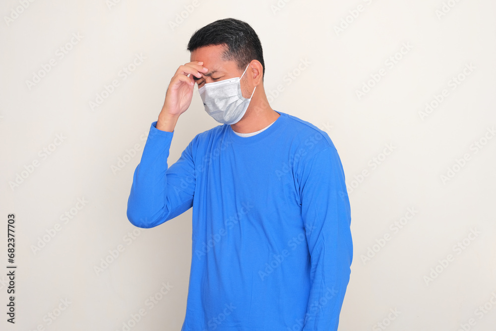 Adult Asian man wearing medical mask suffering headache