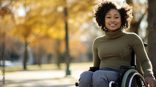 Smiling young woman is sitting in a wheelchair in a park with autumn leaves in the background photo
