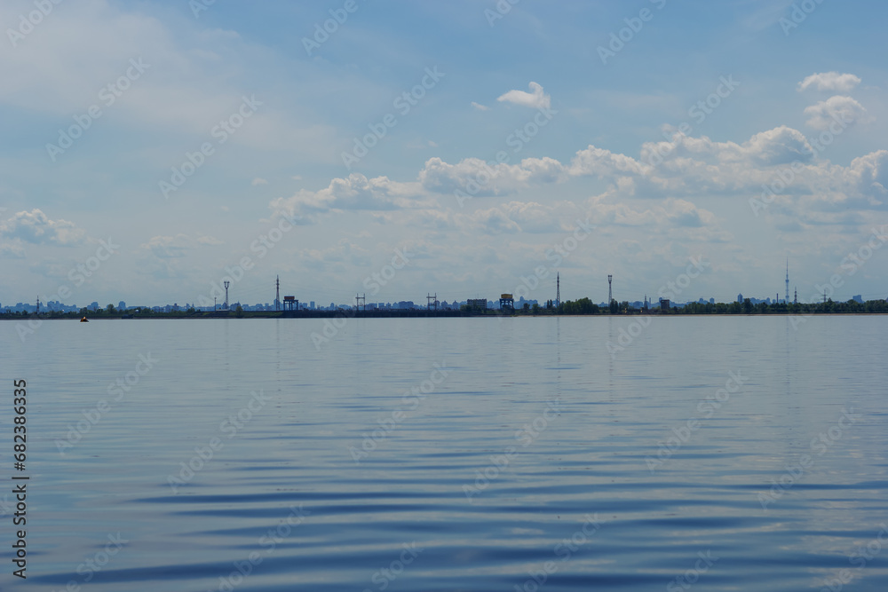 Panoramic view of Kyiv from the lake. City silhouette on the horizon line. Water surface of a lake with traveling waves. Blue water with sun glare and ripples. Kyiv Sea beach. Natural outdoor nature Panoramic view of Kyiv from the lake. City silhouette on the horizon line. Water surface of a lake with traveling waves. Blue water with sun glare and ripples. Kyiv Sea beach. Natural outdoor nature