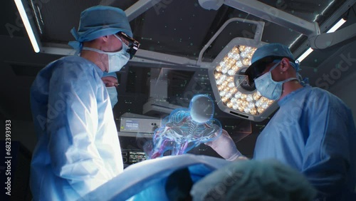 Doctors in AR headsets perform surgery in modern hospital. Surgeons operate patient using 3D virtual hologram showing human organs and skeleton. VFX graphic animation. AI technologies in medicine.