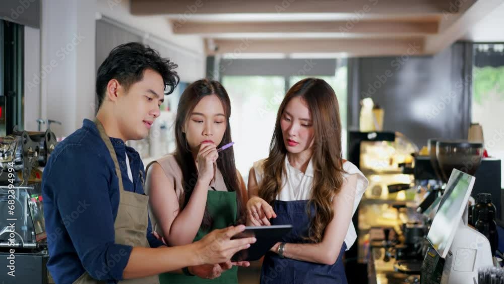 Three barista entrepreneur team meeting at coffee shop. Young Asian male and female cafe employees seriously having discussion with tablet computer Three barista entrepreneur team meeting at coffee shop. Young Asian male and female cafe employees seriously having discussion with tablet computer