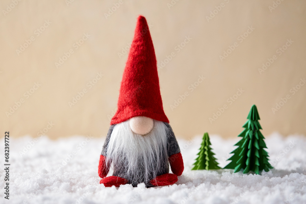 christmas, decoration and winter holidays concept - close up of gnome toy and fir trees made of green paper on artificial snow on beige background christmas, decoration and winter holidays concept - close up of gnome toy and fir trees made of green paper on artificial snow on beige background