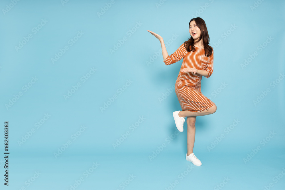 Happy Asian woman presenting or showing open hand palm with copy space for product isolated over blue sky background, Full body composition