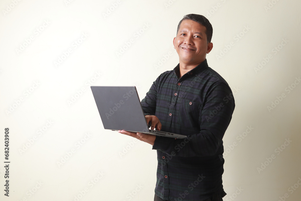 Asian mature man looking at the camera while holding a laptop and showing a very happy expression Asian mature man looking at the camera while holding a laptop and showing a very happy expression